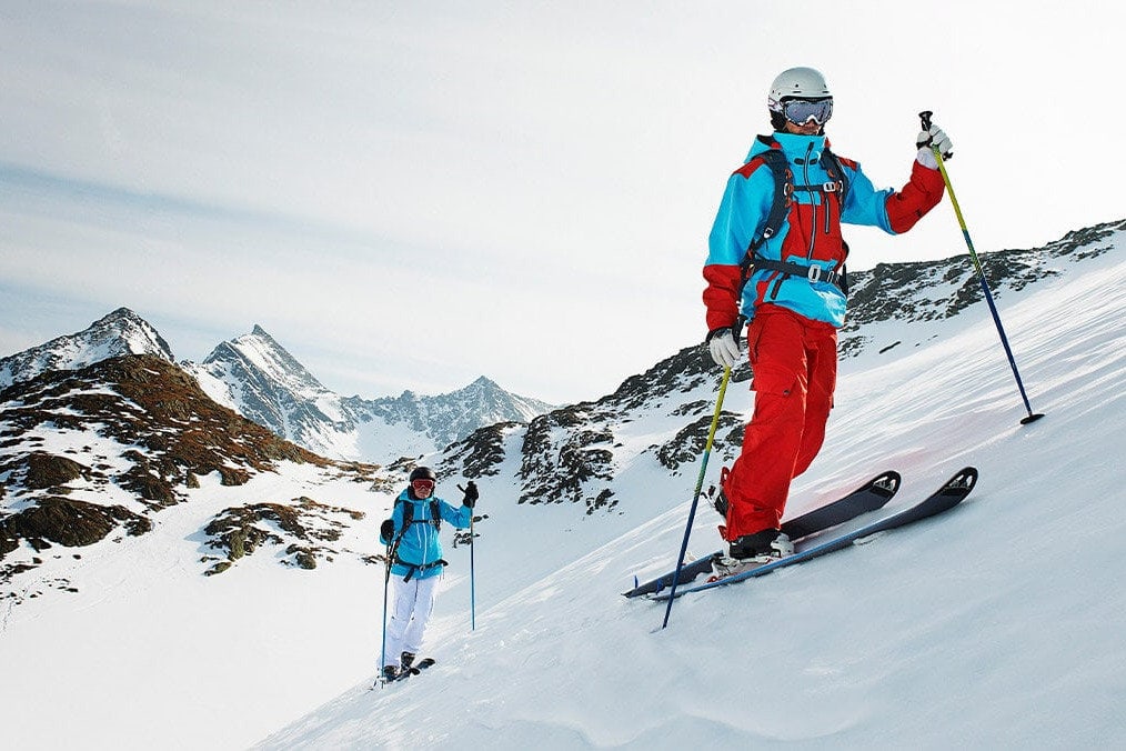 two men traversing uphill on skis