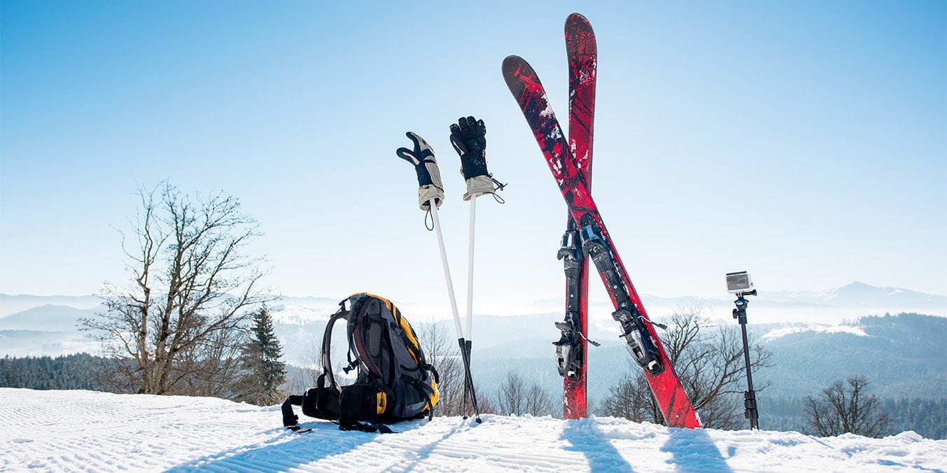 ski stood up in the snow with poles and backpack on the ground, with mountains in the background